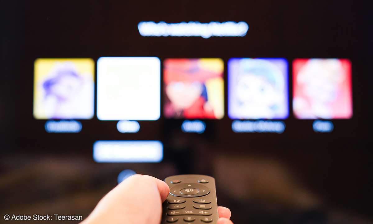 Hand hält Fernbedienung vor einem Fernseher mit Netflix-Login-Bildschirm