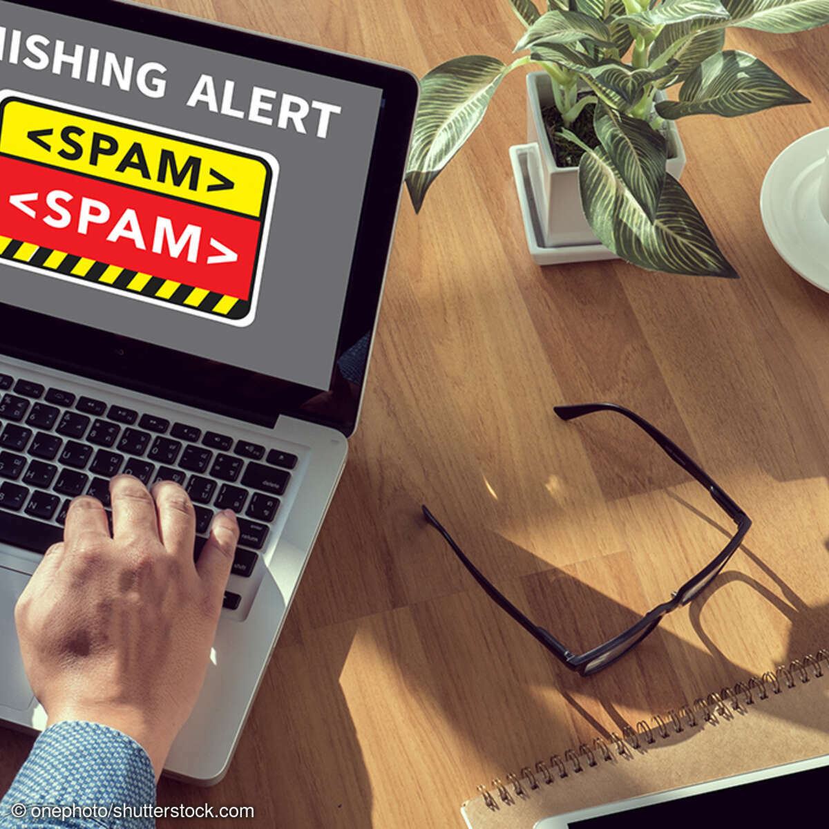 Mann tippt auf Laptopm, auf dem Bildschirm ist eine Phishing-Warnung zu sehen