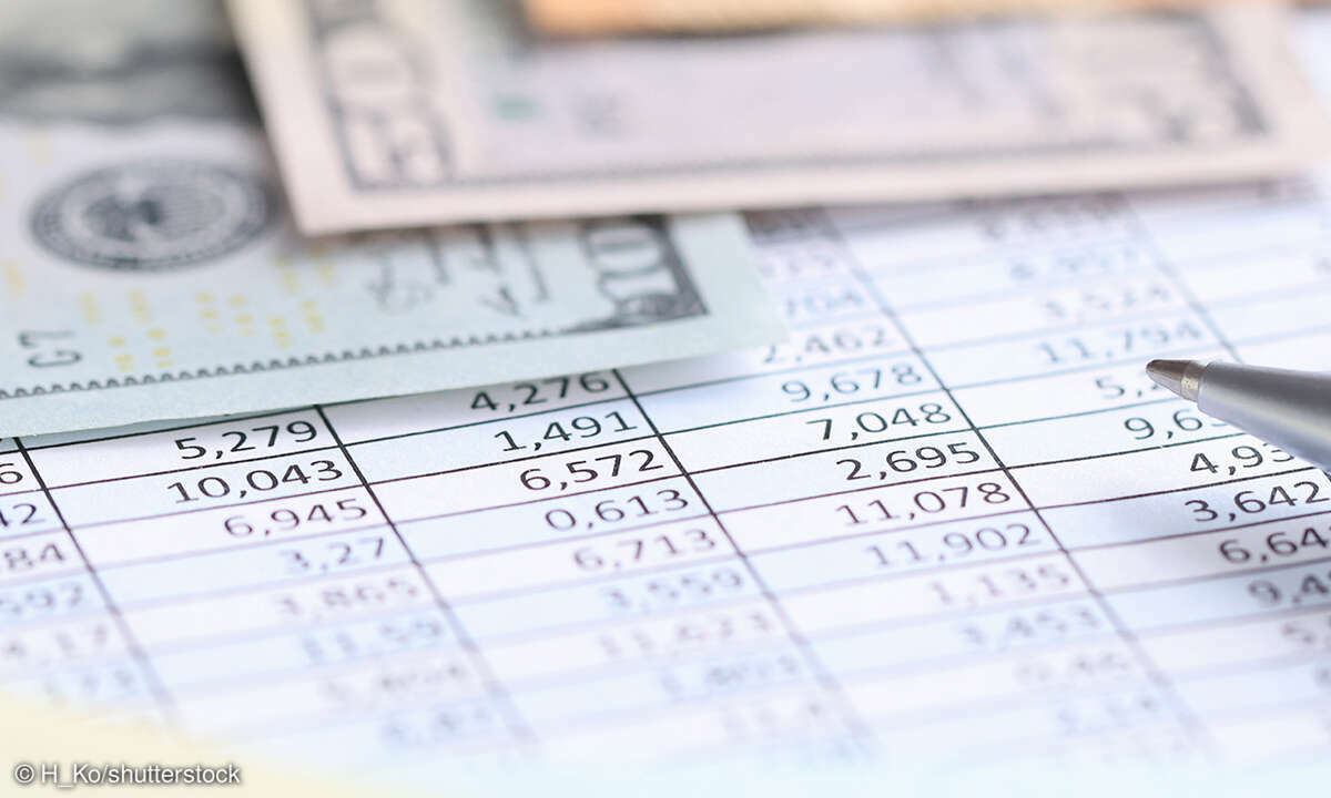 Ein Kugelschreiber zeigt auf Zahlen in einer Tabelle mit Geld auf dem Tisch. 