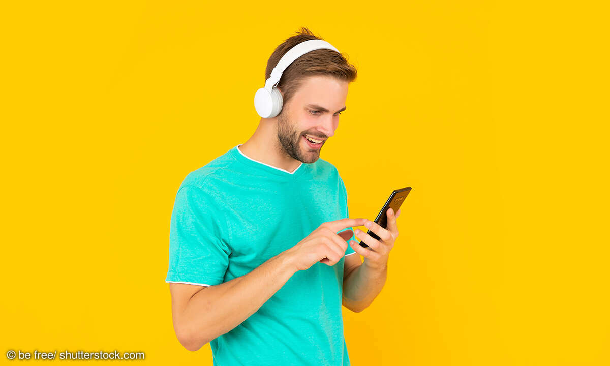 Glücklicher junger Mann, der eine SMS auf seinem Mobiltelefon schreibt und dabei digitale Musik mit Kopfhörern hört,
