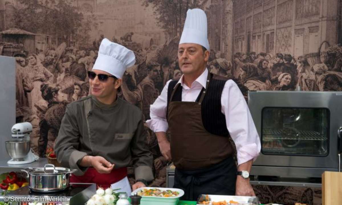 Da Jacky (Michael Youn, links) befürchtet, seine Freundin könnte ihn erkennen, assistiert er Alexandra (Jean Reno) in dessen Kochshow incognito.